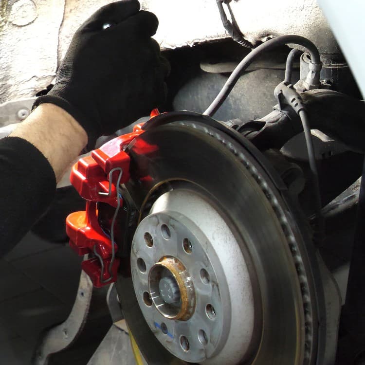 Technician fitting a red brake caliper over the rotor